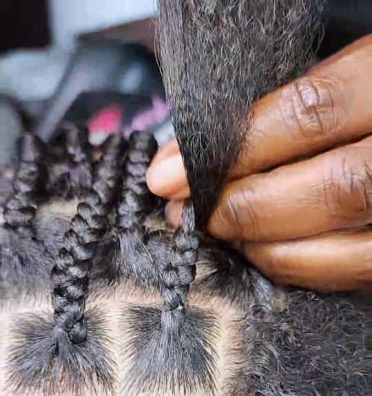Close-up of extension hair being fed into a knotless braid at the root